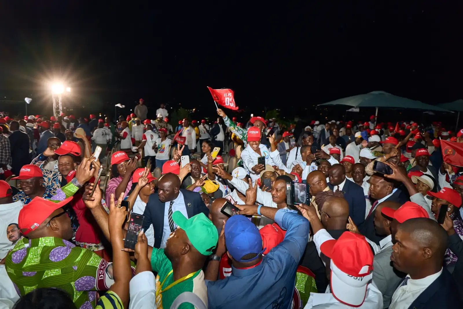 Foule dense en casquettes rouges lors d'un meeting nocturne, téléphones levés au-dessus des têtes.