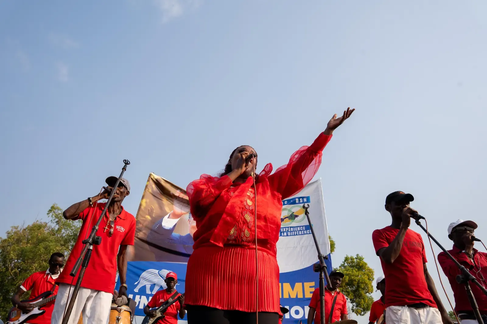 Groupe de musiciens et une chanteuse vêtue de rouge sur une scène, en plein jour.