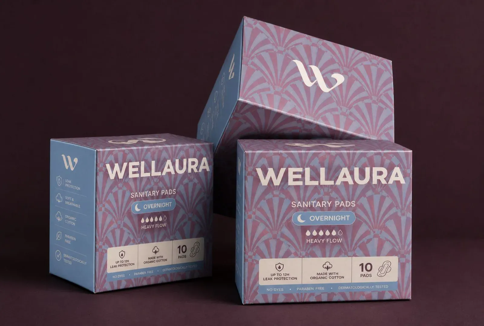 Trois boîtes « Wellaura Sanitary Pads Overnight » au motif géométrique bleu et prune, posées sur un fond aubergine.