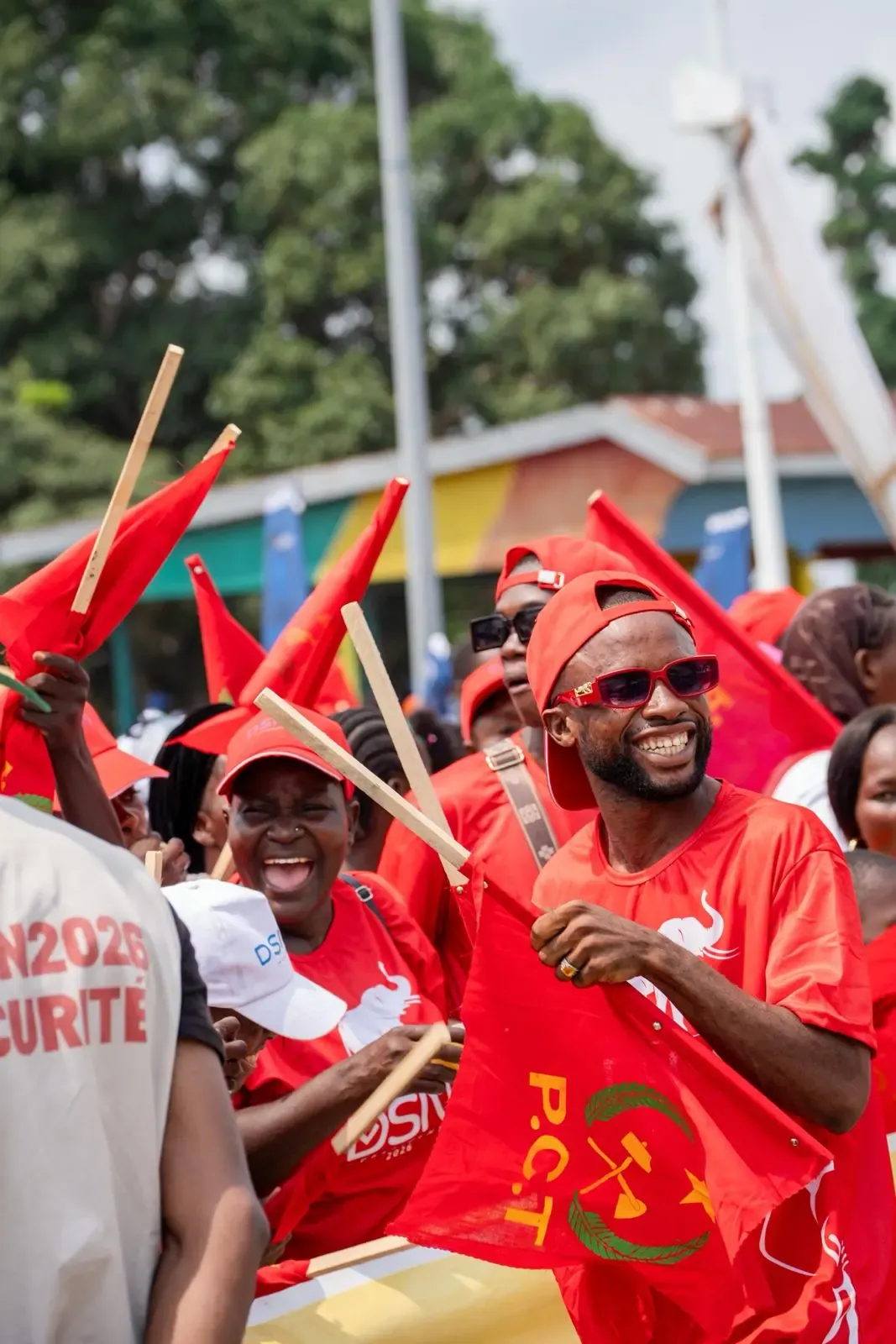 Militants souriants vêtus de rouge, agitant drapeaux et bâtons en plein jour.