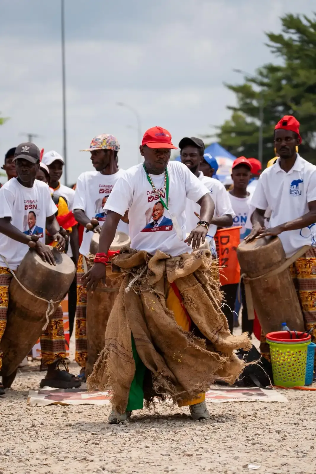Percussionnistes traditionnels et un danseur en costume de raphia dans la rue.
