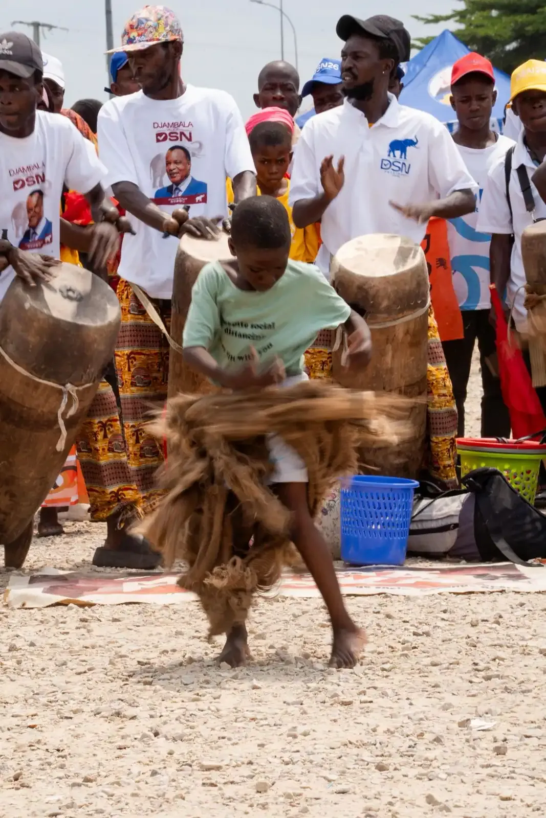 Un enfant danseur en costume de raphia évoluant devant les tambours.